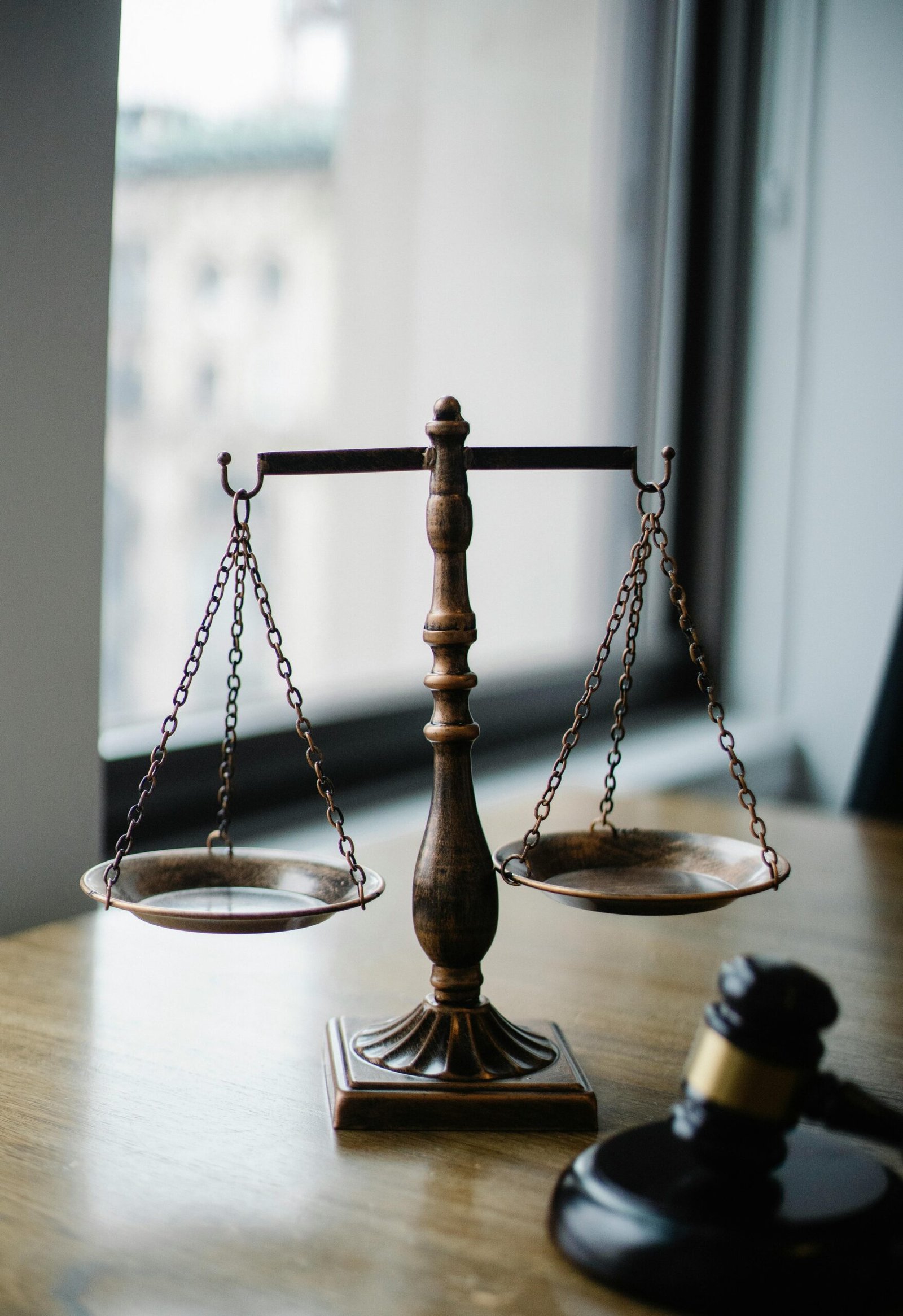 Decorative judgement scale and gavel placed on desk in light lawyer office against window