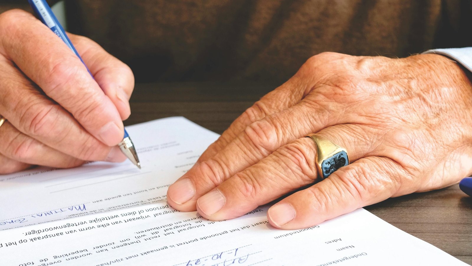 Close-up of a senior adult signing a legal document with a focus on hand and gold ring.